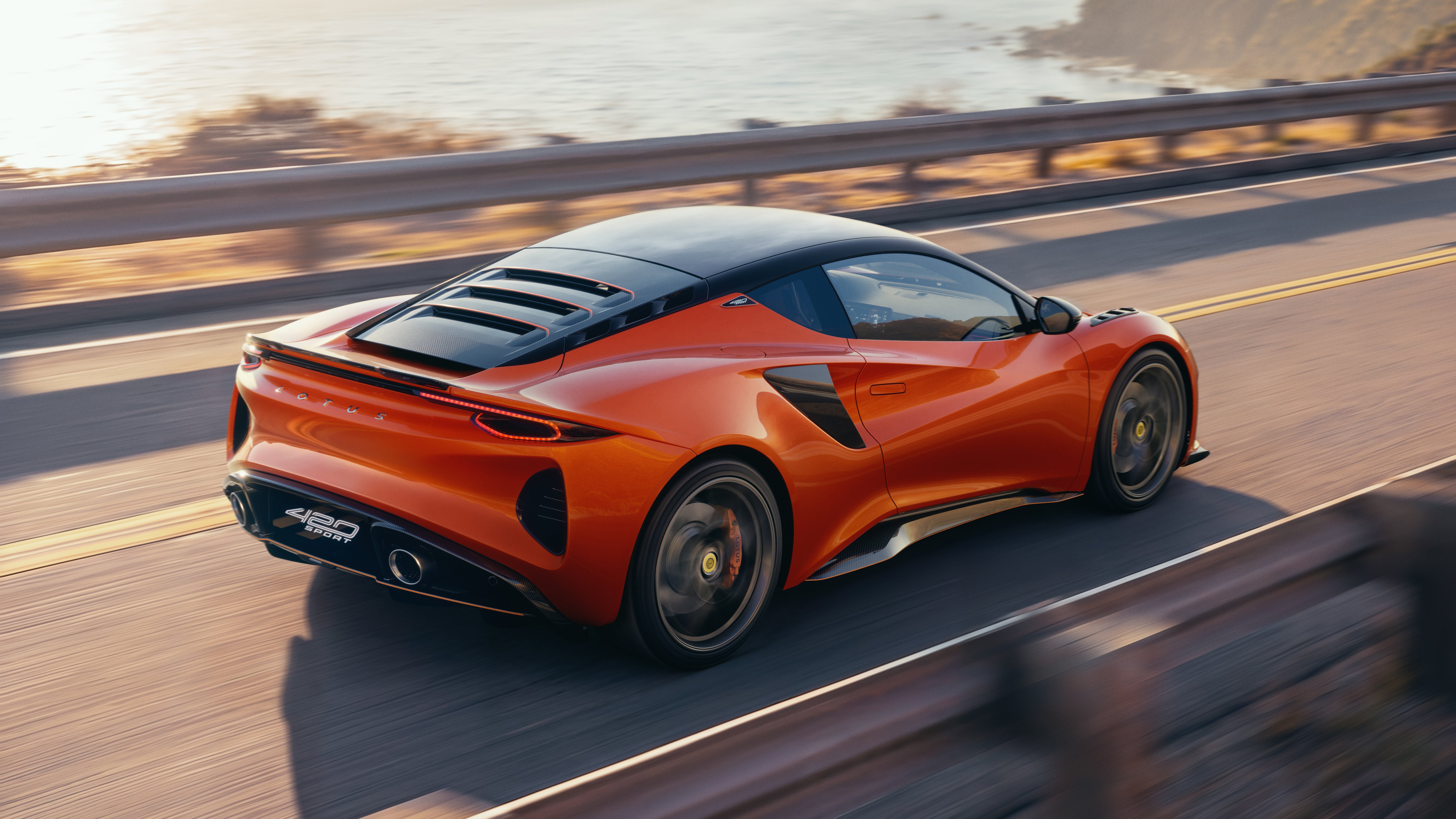 Nuova Lotus Emira 420 Sport Tangelo Orange vista posteriore in dinamica su strada costiera
